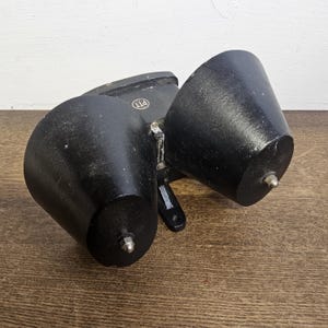 Könnte beinhalten: Eine schwarze Doppelglocke aus Metall mit einem runden, erhabenen, silbernen Etikett mit der Aufschrift "PTT".