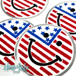 May include: Four round embroidered patches with a smiling face design. The patches are white with red and blue stripes, and the smiling face is black. The patches are surrounded by a silver trim.