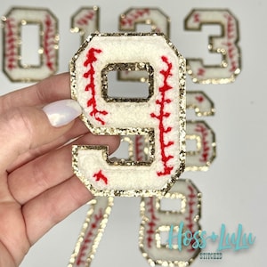 May include: White felt baseball jersey numbers with red stitching and gold glitter trim. The numbers are 0, 1, 2, 3, 7, 8, and 9.