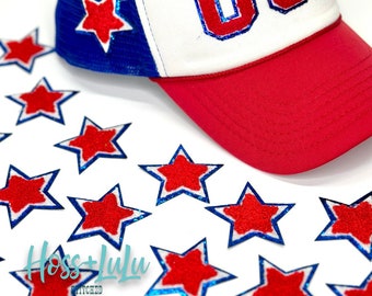 May include: A red, white, and blue trucker hat with the word "USA" embroidered on the front. The hat is surrounded by red, white, and blue star-shaped patches.