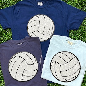 May include: Three t-shirts with a white volleyball design. The shirts are navy blue, dark blue, and light blue.