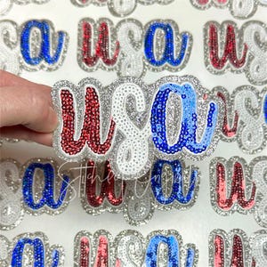 May include: Close-up of a variety of fabric patches with the letters "USA" in red, white, and blue sequins. The patches are arranged in a random pattern and are all the same size.