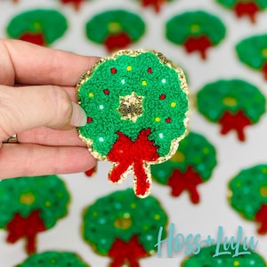 May include: A green Christmas wreath with a red bow and gold glitter. The wreath is decorated with red and white berries and a gold star in the center.