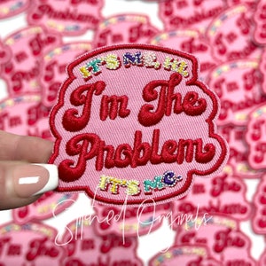 May include: Pink embroidered patch with the text "I'm the Problem It's Me" in red and white thread. The patch is surrounded by a border of colorful beads.