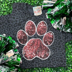 May include: A black and grey leopard print t-shirt with a large pink sequined paw print design.