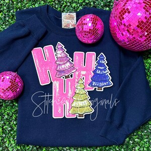 May include: A navy blue sweatshirt with the word "Ho Ho Ho" in pink sequins and three sequined Christmas trees in pink, green, and blue.
