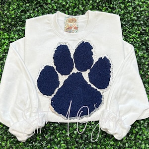 May include: White long-sleeved sweatshirt with a navy blue paw print design outlined in silver glitter.