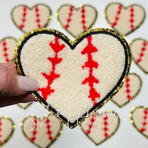 May include: A white heart-shaped patch with a red baseball stitch design and a gold glitter border.
