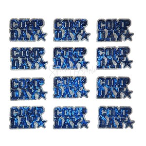 May include: A collection of twelve blue and silver sequined patches. Each patch features the words "COMP DAY" in a bold, blocky font, with a star graphic. The patches are arranged in a grid pattern against a white background.