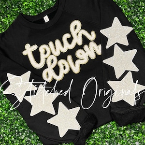 May include: Black sweatshirt with the words "touch down" in gold glitter lettering and four white glitter stars on the sleeves.