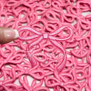 May include: A close-up of a pink satin bow applique. The bow is surrounded by many other pink satin bows.