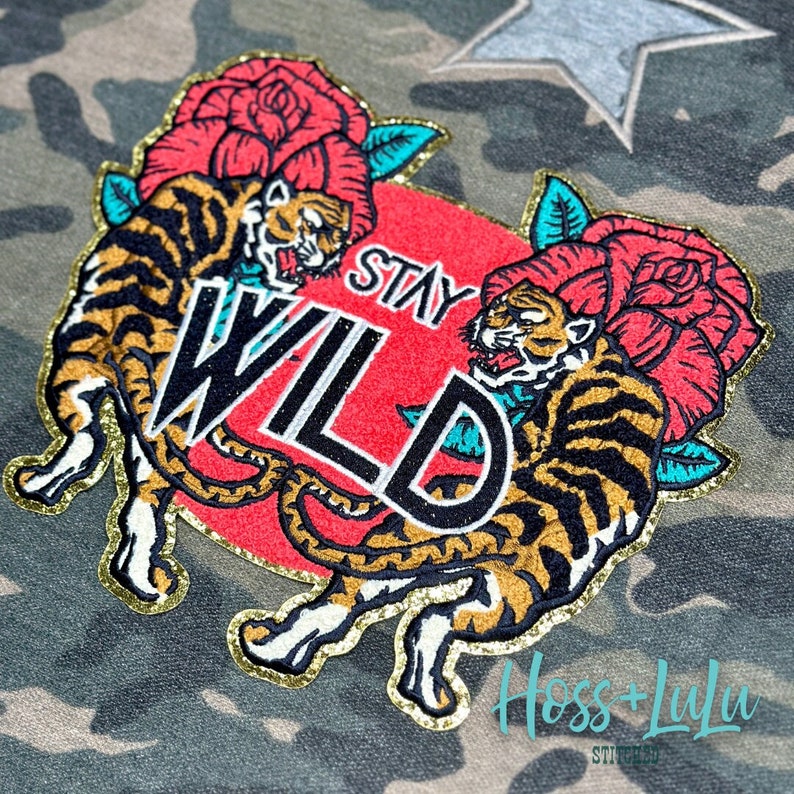May include: Embroidered patch featuring two tigers wearing red roses, a red background with the text "Stay Wild" in white, and a gold glitter outline.