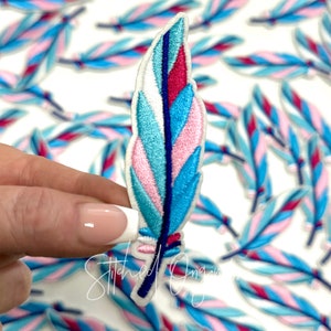 May include: A blue, pink, and white embroidered feather patch. The feather is a popular design for crafts and clothing.