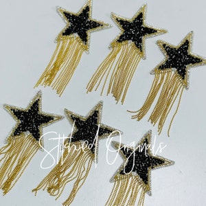 May include: Six black star-shaped patches with gold chain fringe. The stars are embellished with black rhinestones.