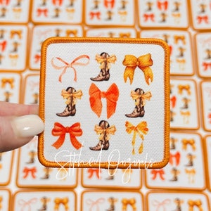 May include: A white fabric patch with an orange border featuring a repeating pattern of orange bows, yellow bows, and brown cowboy boots. The text "Stitched Originals" is printed in the bottom center of the patch.