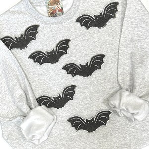 May include: A gray sweatshirt with black bat appliques. The bats are scattered across the front of the sweatshirt.