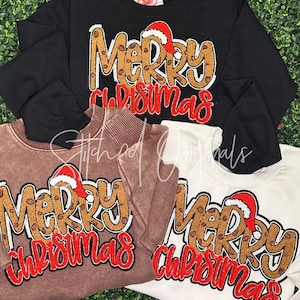 May include: Three sweatshirts in black, brown, and white, each featuring the text "Merry Christmas" in a festive design. The text is in a leopard print style with a Santa hat on top. The sweatshirts are displayed on a green background.