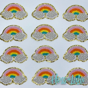 May include: Twelve rainbow-colored felt patches with white pearl-like embellishments. Each patch features a rainbow with pink, orange, yellow, green, blue, and purple stripes. The patches are outlined in gold glitter.
