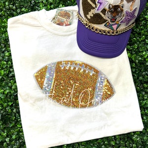 May include: White t-shirt with a gold and silver sequined football design.
