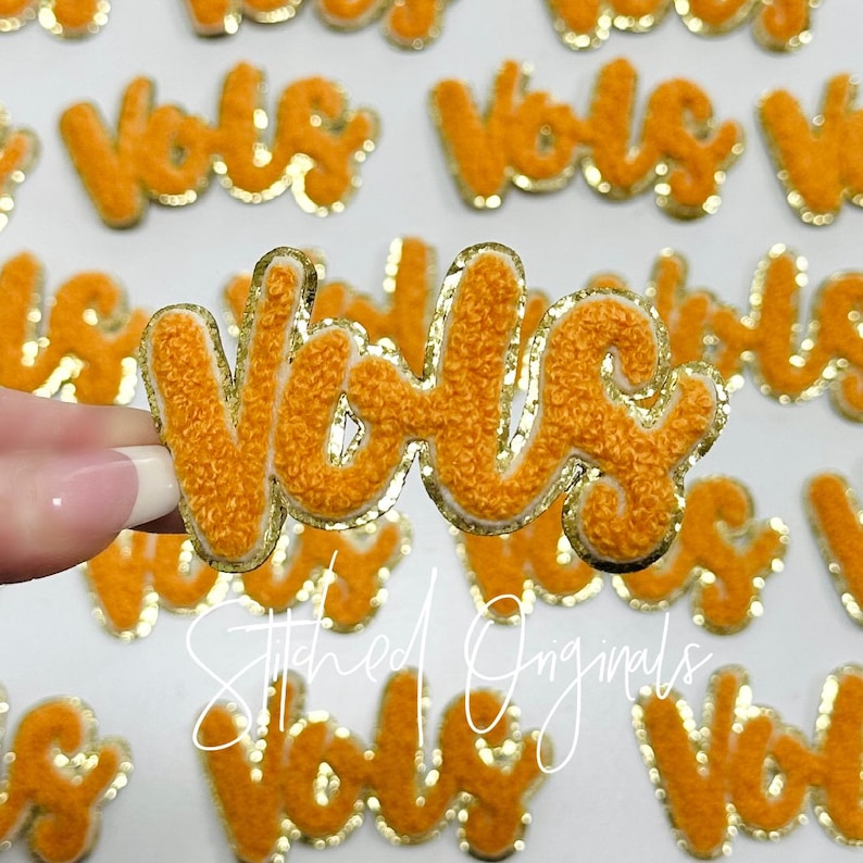 May include: Multiple orange and gold embroidered iron-on patches with the word "Vols" in a cursive font.
