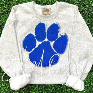 May include: Gray sweatshirt with a large blue paw print with silver glitter around the edges. The paw print is made of a fuzzy material.