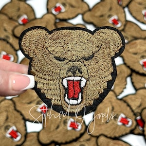 May include: A brown embroidered bear face patch with a red open mouth and white teeth. The bear has a fierce expression.