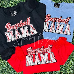 May include: Three shirts with the text "Baseball Mama" in red and white letters with a baseball stitch design. The shirts are black, red, and light blue.
