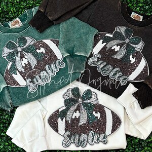 May include: Three sweatshirts with a green, white, and brown football design with a green bow on top. The football has the word "SUGARS" written on it.