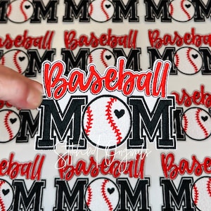May include: Embroidered patch with the words "Baseball MOM" in red and black. The baseball has a heart and red stitching. The patch is white with a black border. The background has multiple patches with the same design.