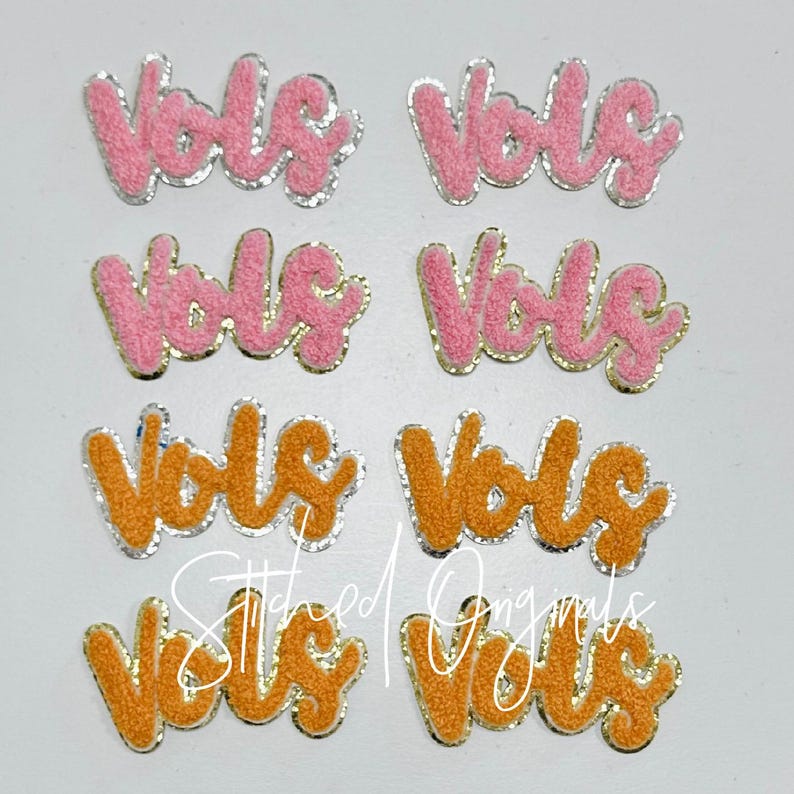 May include: Eight iron-on patches with the word "vols" in a cursive font. Four patches are pink with silver glitter trim and four patches are orange with gold glitter trim.