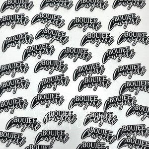 May include: A close-up of multiple black and white iron-on patches with the text "BOUJEE COWGIRL" repeated on each patch.