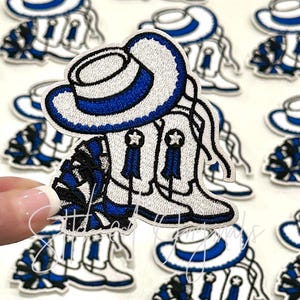 May include: White and blue embroidered iron-on patch featuring a cheerleader wearing a white hat with a blue band, white boots, and a black and white pom-pom.