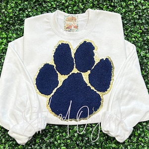 May include: White sweatshirt with a large blue paw print outlined in gold glitter.