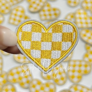 May include: A yellow and white checkered heart-shaped patch. The patch is made of felt and has a stitched edge.