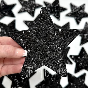 May include: Black sequin star-shaped patches. The patches are covered in small, shiny black sequins. The patches are arranged on a white background. The text "Stitched Originals" is visible on the bottom of the image.