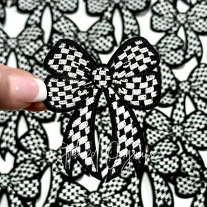 May include: A black and white checkered bow with a satin finish. The bow is a fabric applique and is perfect for adding a touch of style to clothing, bags, or other crafts.