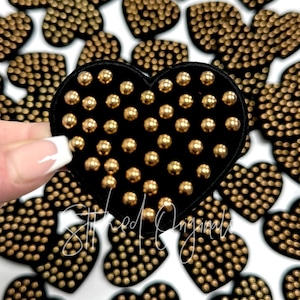 May include: Black felt heart-shaped patch with gold-colored round embellishments. The patch is surrounded by other similar patches.