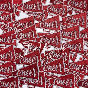May include: A collection of red glitter megaphone patches with the word "Cheer" in silver script. The patches are scattered across a white background, creating a festive and energetic design.