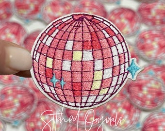 May include: A pink and white embroidered iron-on patch of a disco ball with a glittery design. The patch is surrounded by other similar patches.