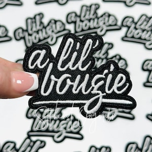 May include: Black and white embroidered patch with the phrase "a lil' bougie" in a cursive font. The patch has a black border and white stitching. The background features multiple similar patches.