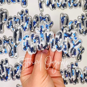 May include: Close-up of multiple sequined "Panthers" patches. The patches feature silver, white, and blue sequins, with a silver border. The patches are in a cursive font. The text "Stitched Originals" is also visible.