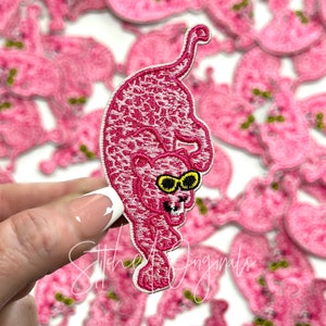 May include: Pink panther patch with a leopard print design and sunglasses. The patch is embroidered and has a white outline.