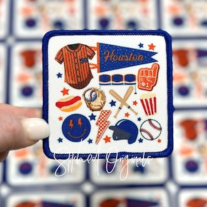 May include: A white iron-on patch with a blue border featuring a baseball theme. The patch includes a baseball jersey, a pennant that says "Houston", a baseball bat and glove, a hot dog, popcorn, and a smiley face with lightning bolts.