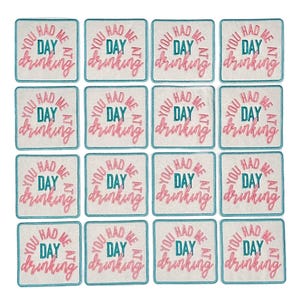 May include: Set of 12 square coasters with a white background and a teal border. The coasters feature pink text that reads "You had me at day drinking".