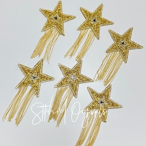 May include: Six gold star-shaped embellishments with beaded detailing and dangling gold chain fringe. Each star has a small black or clear gem in the center. The text "Stitched Originals" is visible in the image.