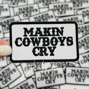 May include: A white embroidered patch with black stitching that reads "Makin Cowboys Cry". The patch is surrounded by other similar patches.