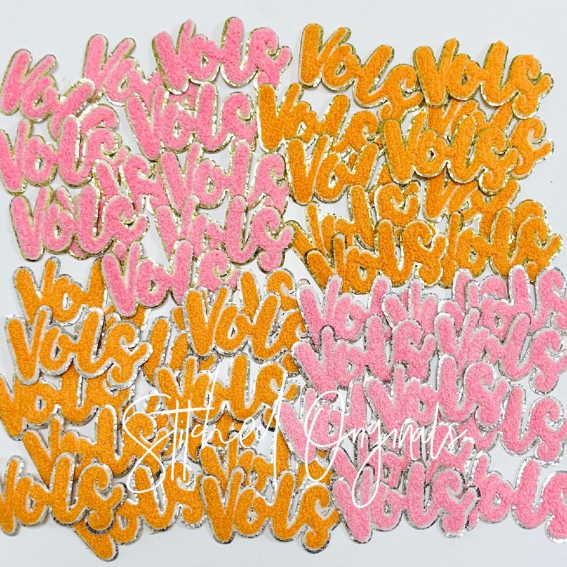 May include: A large pile of pink and orange felt patches with the word "Vote" written on them in a cursive font. The patches have a silver outline and are covered in glitter.