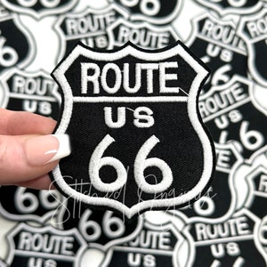 May include: A black and white embroidered patch with the text "ROUTE US 66" in a white shield shape.