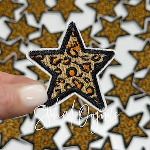 May include: A close-up of a leopard print star-shaped iron-on patch. The patch is black with orange and brown leopard print. The patch is surrounded by other star-shaped patches.