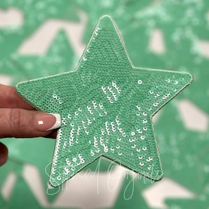 May include: A green star-shaped patch covered in sequins. The sequins are a light green color with a silver sheen.